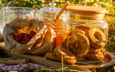 A warm outdoor picnic with herbal tea, rose hips, honey, lemon, and cookies set in a sunny meadow, creating a cozy, natural, and rustic atmosphere.