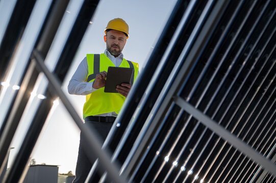 Man standing among photovoltaic panels analyzing data on digital tablet