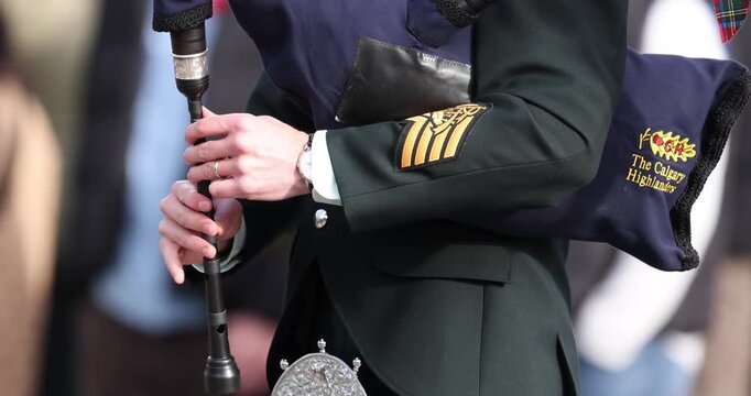 Close-up of a Calgary Highlanders bagpiper playing the chanter, displaying the embroidered regimental name on the blue bag cover.