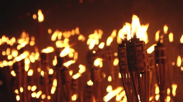 Close-up of a single lit bamboo torch with many others glowing in the blurred background, creating a warm and intense flame-filled atmosphere.
