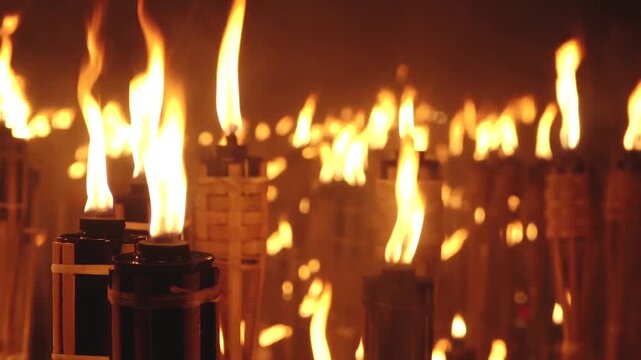 Close-up of a single lit bamboo torch with many others glowing in the blurred background, creating a warm and intense flame-filled atmosphere.