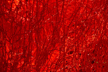 A mesmerizing tangle of red threads forms a dense, abstract web. Light glints off the fibers, enhancing the texture and depth, evoking emotion, complexity, and artistic entanglement.