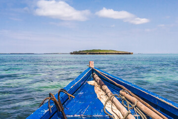 A traditional wooden boat with blue painted planks and a removable mast and furled sail. 