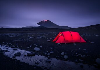 Illuminated red tent set up in volcanic landscape under a dark moody sky