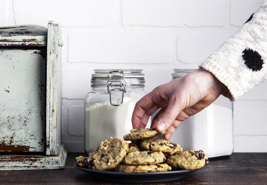 Close up of human hand taking a chocolate chip cookie from the plate.