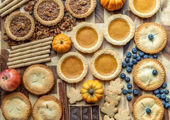 Fall dessert assortment includes pumpkin pie, pecan pie, and seasonal fruits on wooden surface