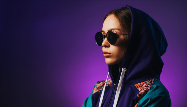 Nastolatka w stylowych okularach przeciwsłonecznych i bluzie z kapturem na fioletowym tle