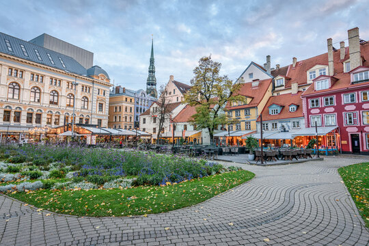 A large city square in Riga, historic buildings, cafes and cobbles, with planted flower beds. 