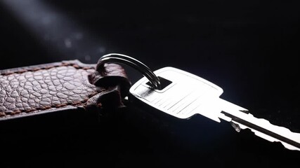 Key with Leather Fob - A close-up shot shows a silver key attached to a brown leather key fob. The key and fob are illuminated against a dark background with subtle light flares. - Powered by Adobe