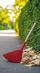Broom rests on sidewalk beside green hedges during a sunny day in an urban park setting