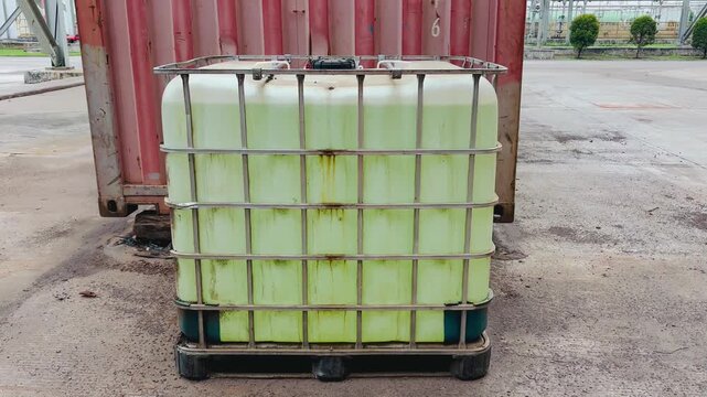 Intermediate bulk container filled with a greenish-yellow chemical liquid, sitting on a pallet in an industrial storage area
