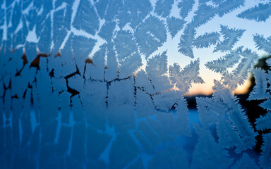 Intricate frost patterns forming on a window pane during winter