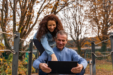 Happy mature couple smiling together, using a small laptop in an autumn park