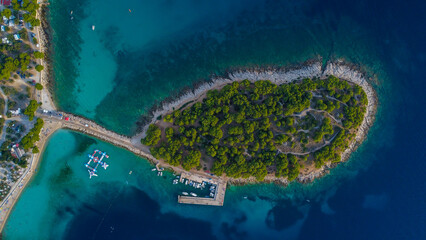 High-angle aerial drone shot of a small forested island with a recreational harbor, inflatable...