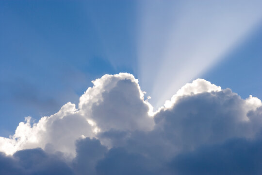 Sun shining behind cumulonimbus clouds in a blue sky. 