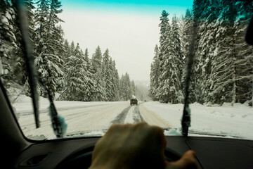 Driver's view through the windscreen of a snowy road and cars driving, a driver's hand on the wheel. 