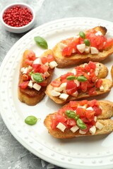 Tasty bruschettas with mozzarella cheese, tomatoes, basil and peppercorns on grey textured table, closeup