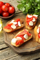 Tasty bruschettas with mozzarella cheese, tomatoes and basil on wooden table