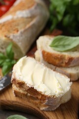 Slices of baguette with butter, basil and knife on wooden table, closeup