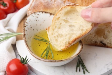 Woman dipping piece of baguette into oil at table, closeup