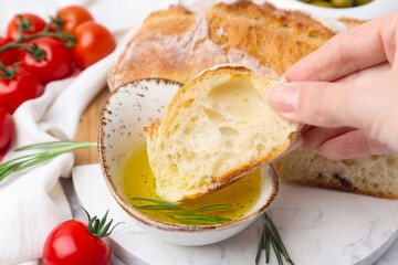 Woman dipping piece of baguette into oil at table, closeup