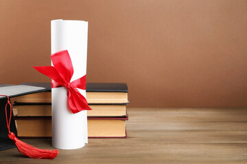 Graduation cap, diploma and books on wooden table against brown background. Space for text