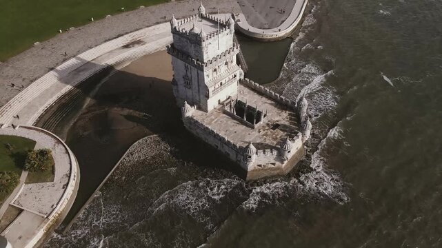 Aerial view of the historic Belem Tower surrounded by the dark, moody waters, contrasting against the adjacent lush green park, Lisbon, Lisbon, Portugal.