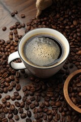 Aromatic coffee in cup and beans on wooden table, closeup