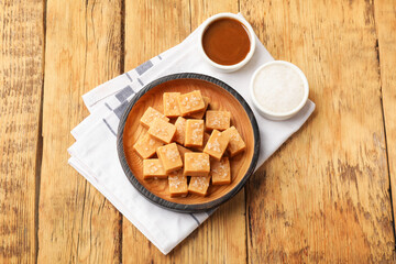 Tasty candies with salt and caramel sauce on wooden table, top view