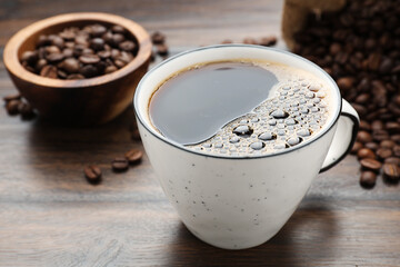 Aromatic coffee in cup and beans on wooden table, closeup