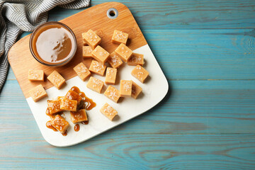 Tasty candies with salt and caramel sauce on light blue wooden table, top view. Space for text