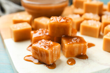 Tasty candies with salt and caramel sauce on light table, closeup