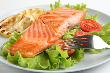 Piece of tasty grilled salmon, lemon slices and salad on white table, closeup