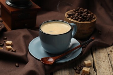Aromatic coffee in cup, beans, brown sugar and grinder on wooden table, closeup