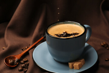 Pouring aromatic coffee into cup, beans and brown sugar on fabric, closeup