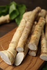Fresh raw horseradish roots and leaves on wooden table, closeup