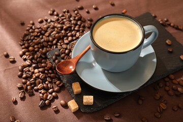 Aromatic coffee in cup, beans and brown sugar on table, closeup. Space for text