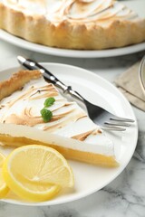Slice of tasty lemon meringue tart with mint served on white marble table, closeup