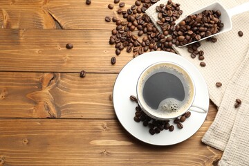Aromatic coffee in cup and beans on wooden table, flat lay. Space for text