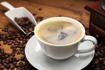 Aromatic coffee in cup, beans and grinder on wooden table, closeup