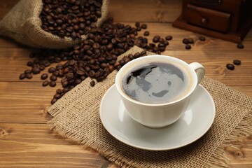 Aromatic coffee in cup, beans and grinder on wooden table, closeup
