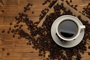 Aromatic coffee in cup and beans on wooden table, flat lay. Space for text