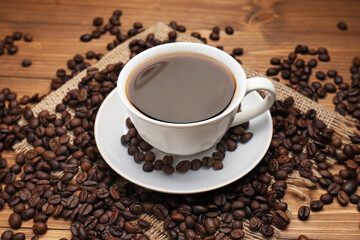 Aromatic coffee in cup and beans on wooden table, closeup