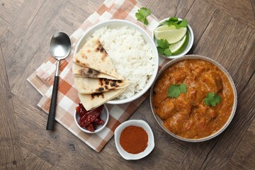 Delicious chicken tikka masala, rice, cilantro, lime, lavash and spices on wooden table, flat lay