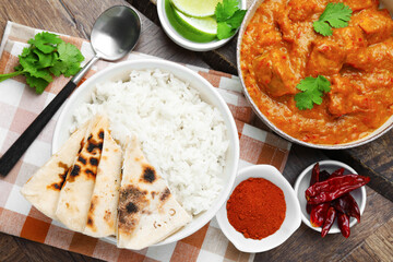 Delicious chicken tikka masala, rice, cilantro, lime, lavash and spices on wooden table, flat lay