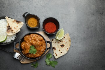 Delicious chicken tikka masala, rice, cilantro, lime, lavash and spices on grey textured table, flat lay. Space for text