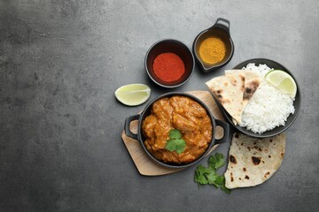 Delicious chicken tikka masala, rice, cilantro, lime, lavash and spices on grey textured table, flat lay. Space for text