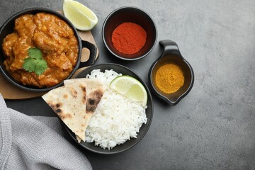 Delicious chicken tikka masala, rice, cilantro, lime, lavash and spices on grey textured table, flat lay. Space for text