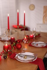 Stylish Christmas table setting with plates, glasses and burning candles in room, closeup