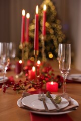 Stylish Christmas table setting with plates, glasses and burning candles in festive decorated room,...